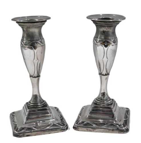 A pair of Edwardian silver candlesticks, decorated with ribbons, etc., on a square base, loaded,...