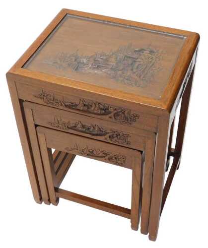 A nest of three mid 20thC Japanese tables, each heavily carved with a scene of figures, boats...