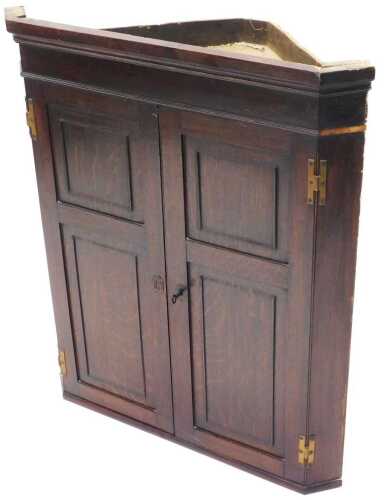 An early 19thC oak panelled hanging corner cupboard, with fitted shelves, 96cm high, 79cm wide,...