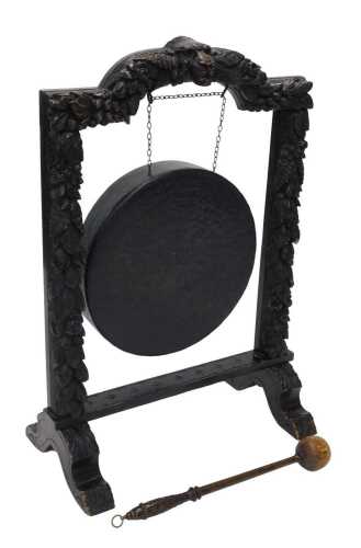 A 19thC oak framed dinner gong, heavily carved with lion's masks surrounded by berries, leaves...