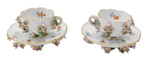 A pair of early 20thC Meissen porcelain cups and saucers, each raised with flowers, on a white...
