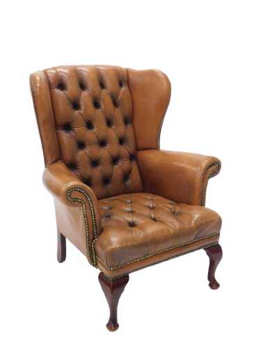 A late 20thC leather wingback fireside chair, with studded back and seat, on cabriole front legs...