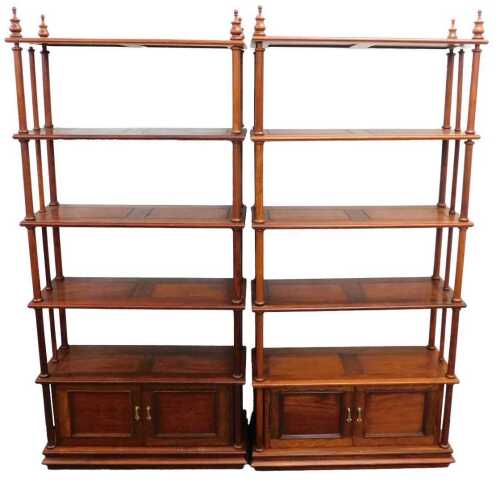 A pair of hardwood open bookcases, each with plain shelves above a cupboard, held by cylindrical...
