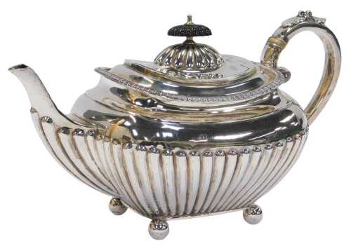 A George V silver teapot, of semi fluted form, raised on four ball feet, with an ebonised knop...
