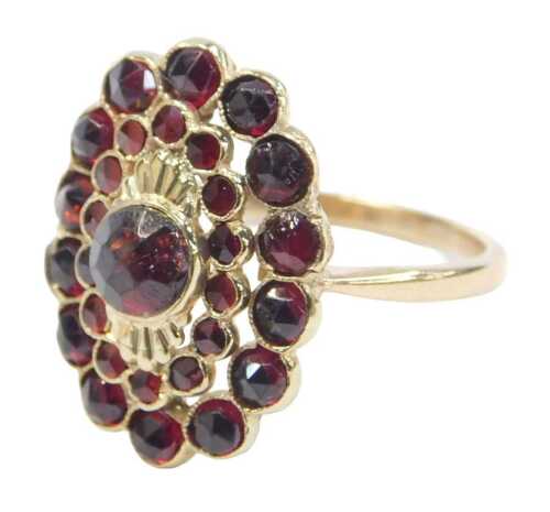 A 20thC garnet dress ring, the halo ring with a central cabochon-cut garnet, surrounded by rough-...