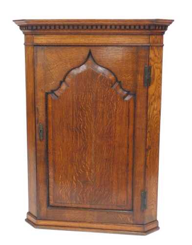 A George III oak hanging corner cupboard, the top with a dentil moulded edge above an arched...