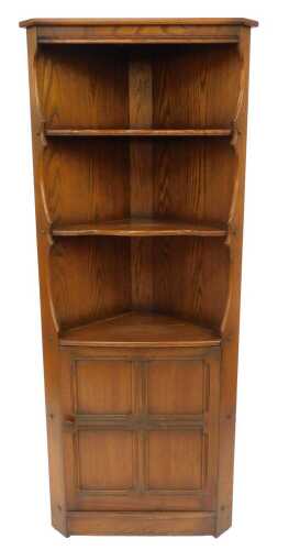 An Ercol Old Colonial elm standing corner cabinet, the top with two shaped shelves above a...