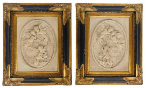 A pair of reconstituted marble plaques, each cast with a depiction of cherubs, within an oval...