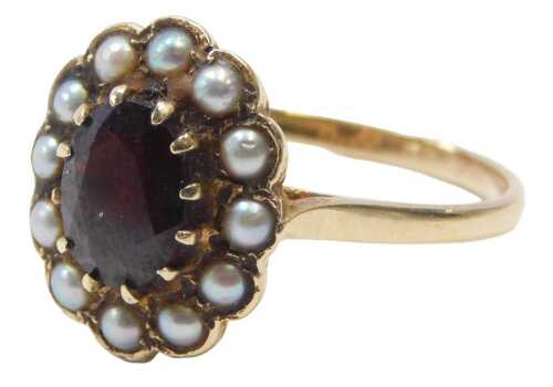 A 9ct gold garnet and seed pearl ring, the central oval garnet in a claw setting, surrounded by...