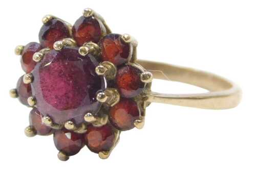 A 9ct gold and garnet flowerhead ring, the layered garnet with central stone surrounded by ten...