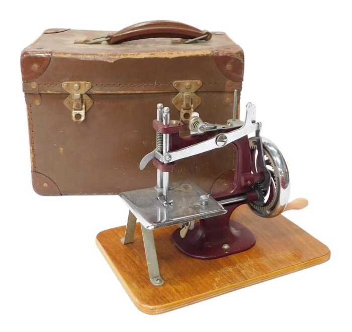 A mid century child's hand operated sewing machine, in purple, 20cm high, cased.