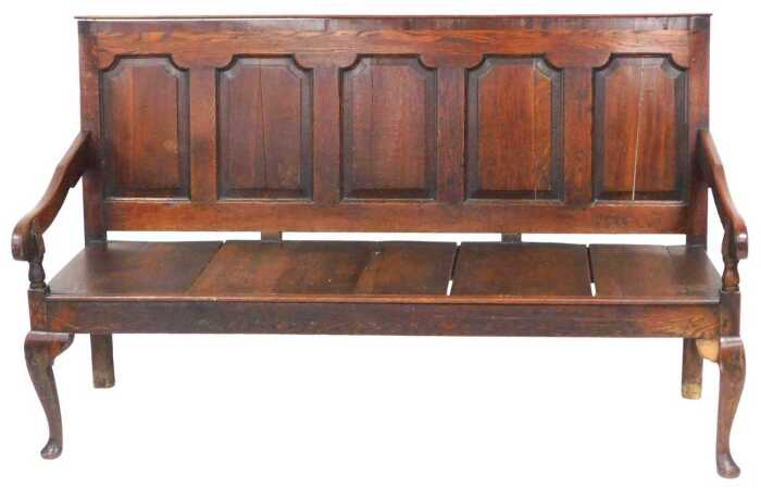 A George III oak settle, with a five panelled back, and solid seat, with outswept...