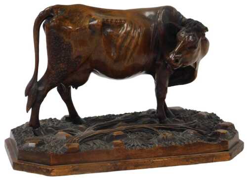 A late 19thC Swiss carved linden wood figure of a cow, modelled standing, on a floral and tree...
