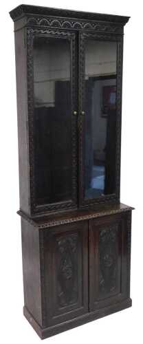 A Victorian carved oak cupboard bookcase, the carved pediment above a pair of glazed doors...