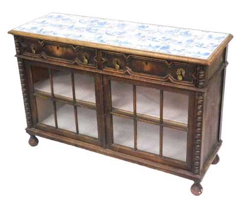 A Victorian oak cabinet, with a Delft blue tile top, of twenty seven tiles, decorated with canal...
