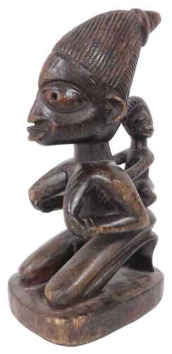 An African Yoruba carved maternity figure, in the form of a female with child on her back, on a...