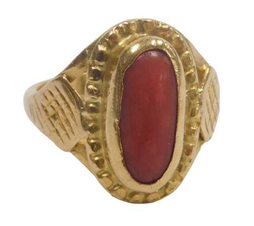 A Continental cabochon coral ring, in an oval setting, with engraved shoulders, yellow metal,...