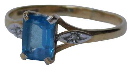 A 9ct gold dress ring, set with a rectangular cut blue topaz, flanked by two tiny diamonds to...