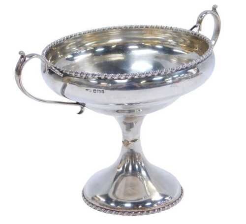 A George V silver twin-handled tazza, with a gadrooned rim, raised on an hourglass stem, on a...