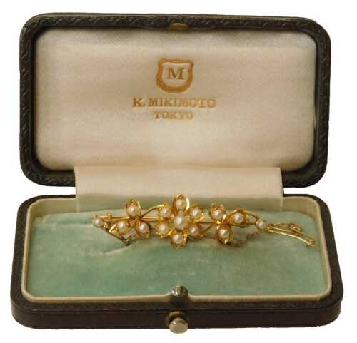 A Mikimoto pearl bar brooch, formed a central flower, with two three-point leaf details, on a...