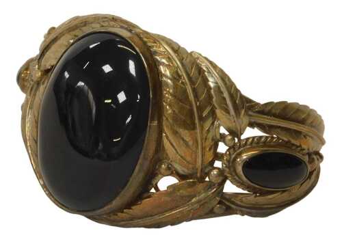 A torc bangle, set with a polished agate central stone, with crossover leaf and vine design,...