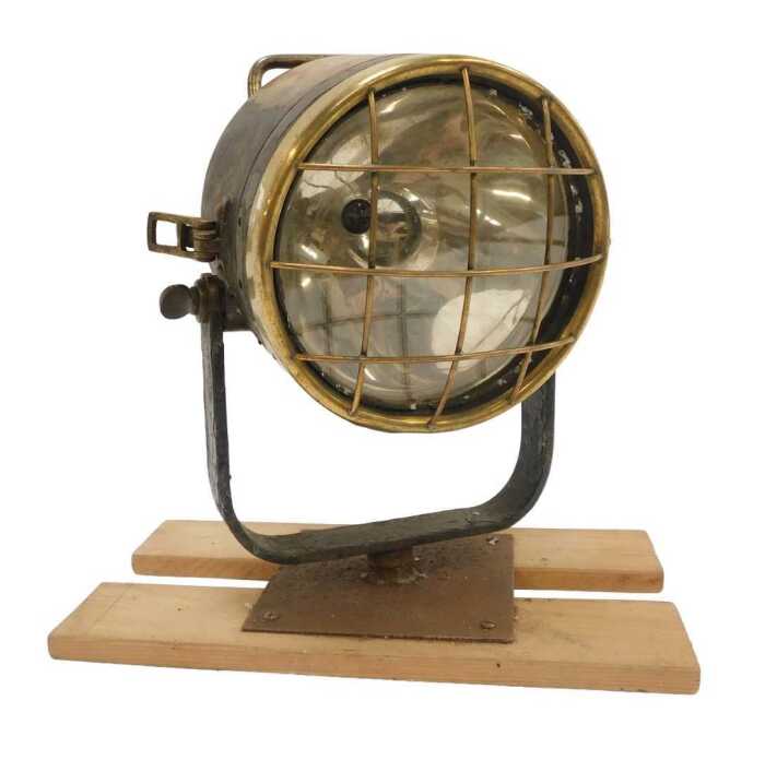 A brass ship's spotlight, mounted on a wooden plinth.