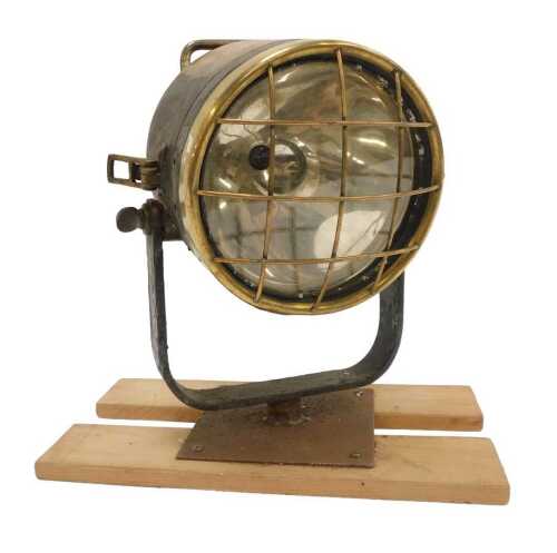 A brass ship's spotlight, mounted on a wooden plinth.