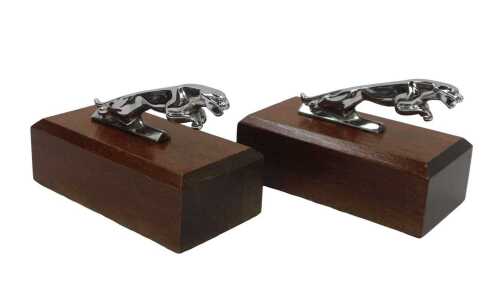 Two Jaguar chrome plated car mascots, each on a mahogany plinth, 16cm wide overall.