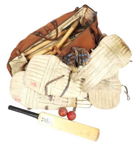 A vintage leather and canvas cricket bag, containing various cricket equipment, to include pads,...