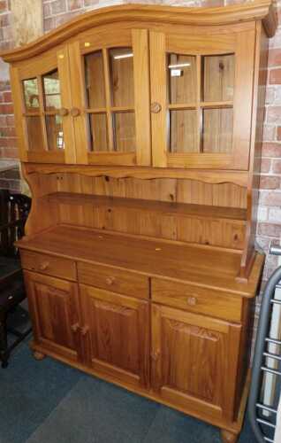 A modern pine finished dresser, with plate rack, three glazed doors to top over shelf, above...