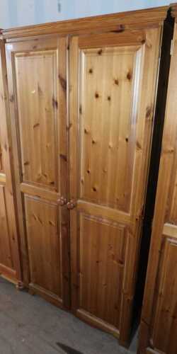 A pine two door wardrobe, doors opening to reveal a hanging rail, raised on bun feet.