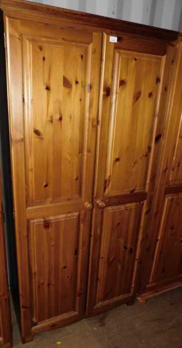 A pine two door wardrobe, doors opening to reveal a hanging rail, raised on bun feet.