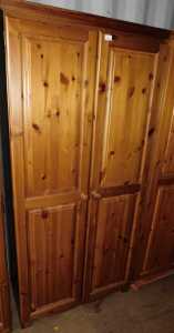 A pine two door wardrobe, doors opening to reveal a hanging rail, raised on bun feet.