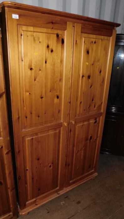 A pine two door wardrobe, doors opening to reveal a hanging rail, raised on bun feet.