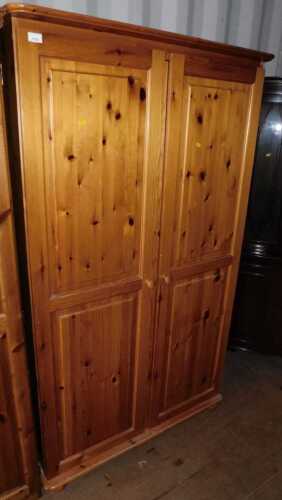 A pine two door wardrobe, doors opening to reveal a hanging rail, raised on bun feet.