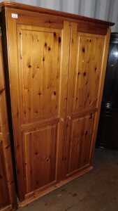 A pine two door wardrobe, doors opening to reveal a hanging rail, raised on bun feet.