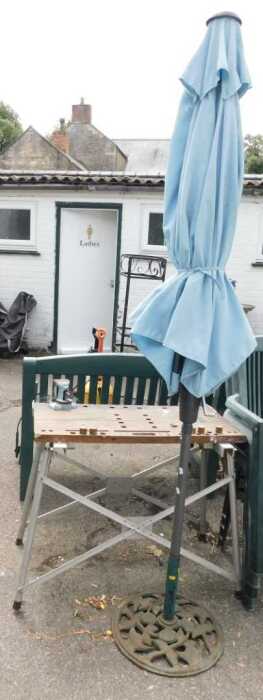 A parasol with a metal base, a work bench with a wooden top, metal base and vice.
