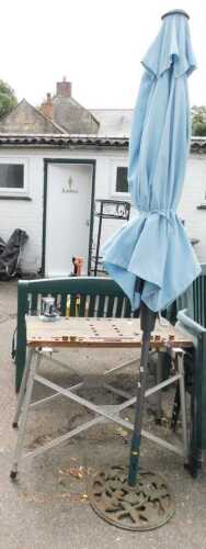 A parasol with a metal base, a work bench with a wooden top, metal base and vice.
