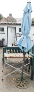 A parasol with a metal base, a work bench with a wooden top, metal base and vice.