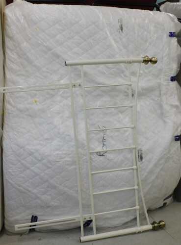 A 56" wide bed surround, comprising metal headboard with white partially wrapped mattress.