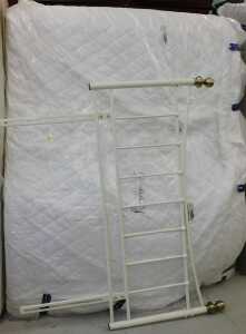 A 56" wide bed surround, comprising metal headboard with white partially wrapped mattress.