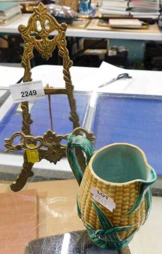 A brass easel book or photograph stand, together with a ceramic jug in the form of an ear of corn.