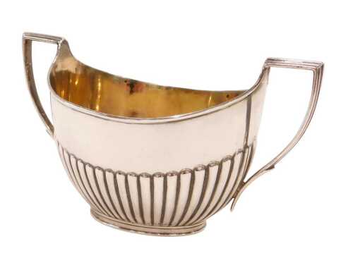 A Victorian silver sugar bowl, of cape form with angular strap handles, partially gadrooned on...