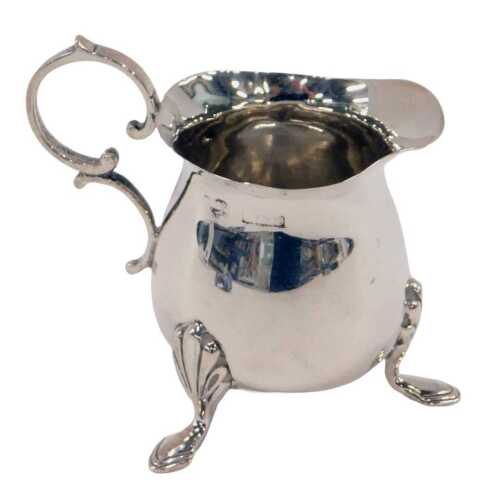 A George V silver cream jug, with ear handled triple stepped hoof feet and plain bulbous body,...