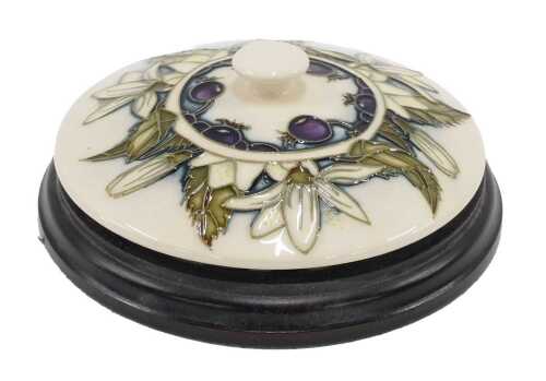 A Moorcroft pottery Juneberry pattern lid, on wooden plinth base, 14cm diameter.