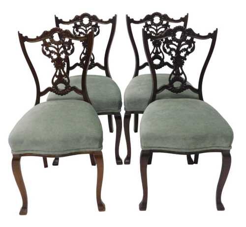 A set of four Victorian walnut salon chairs, each with heavily carved scroll and floral pierced...