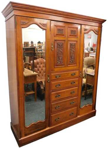 A late Victorian walnut triple wardrobe, the central heavily carved door revealing fitted shelf,...