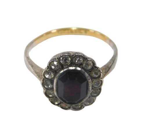 An 18ct gold and silver cluster ring, the oval red paste stone surrounded by a halo of white...