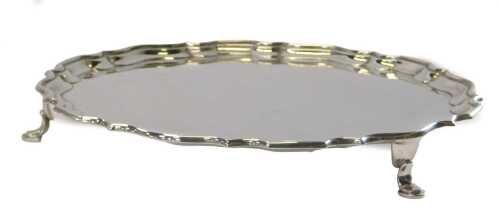 A George V silver salver, of circular form with a piecrust border, raised on three hoof feet,...