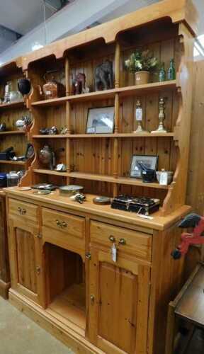 V - A pine kitchen dresser, the upper section with three open shelves, raised above three frieze...